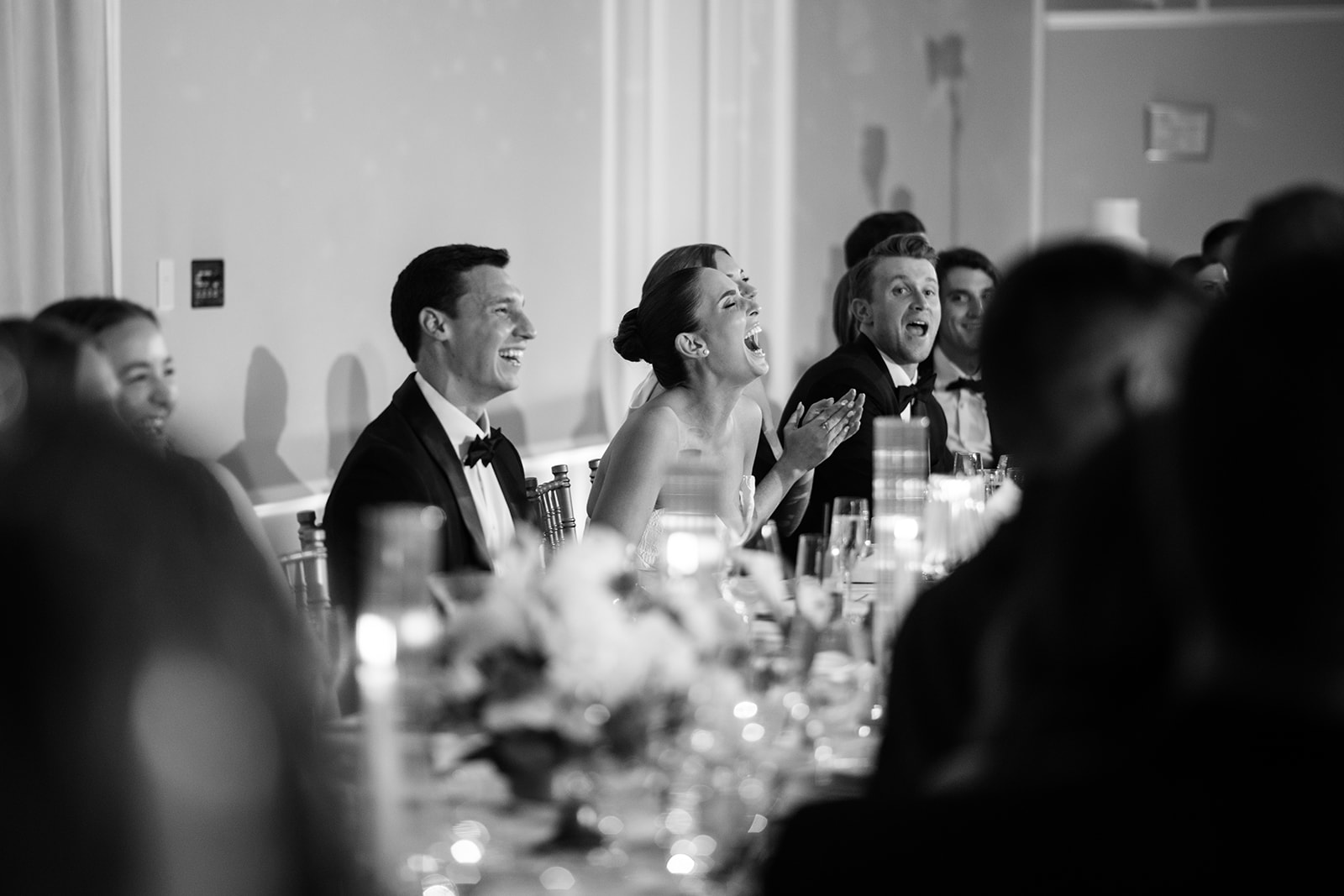 Black and white film photo of the couple laughing hysterically during wedding toasts at the head table.